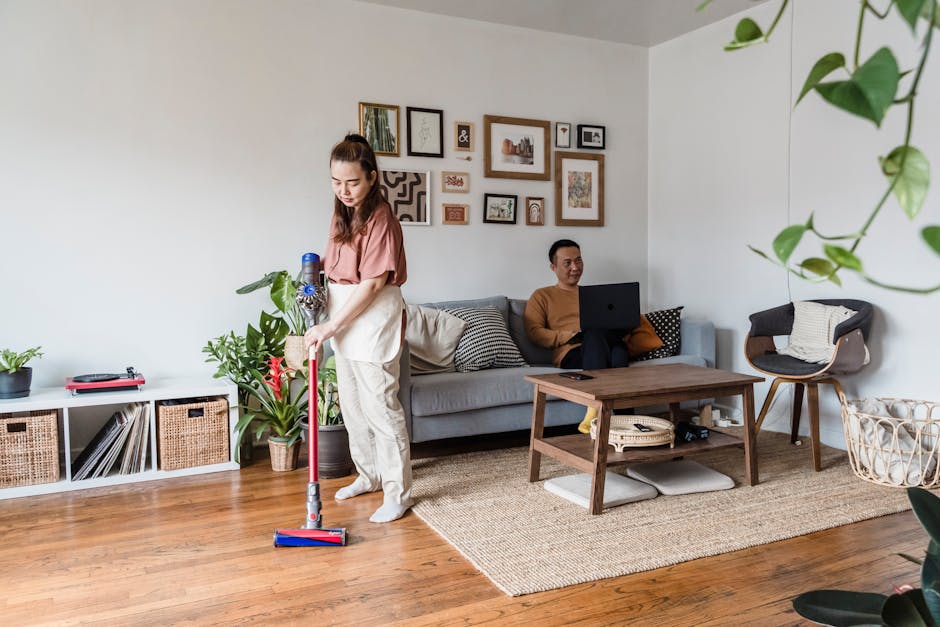 Woman vacuuming while man works remotely on laptop in cozy living room.