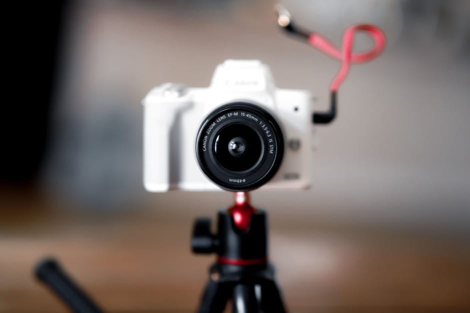 White digital camera mounted on tripod with blurred background.