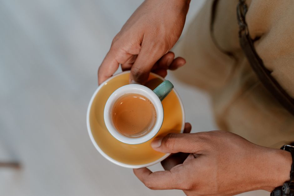 Top view of espresso cup held by hands, set against a soft background.
