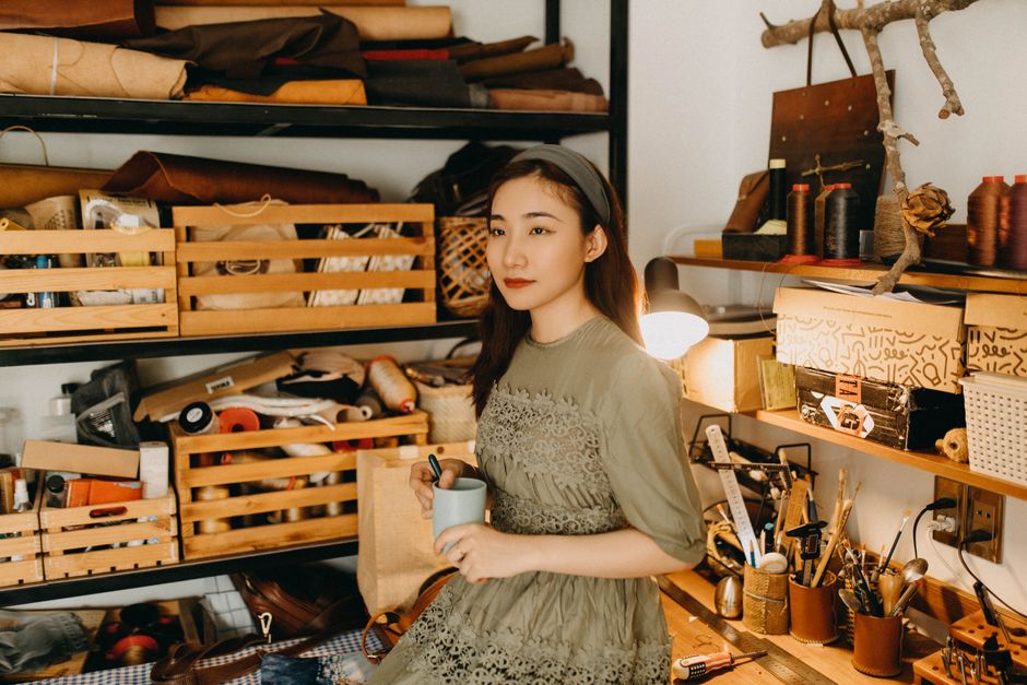Young woman in a home workshop surrounded by crafting materials, holding a mug.