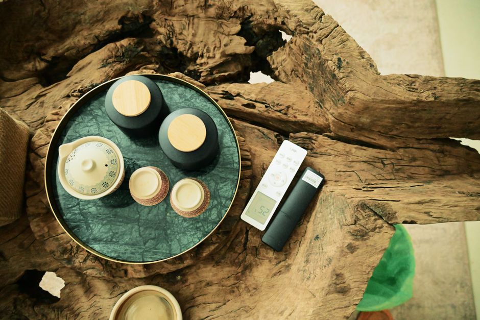 Top view of a tea set arranged on a rustic driftwood table, with a remote control visible.