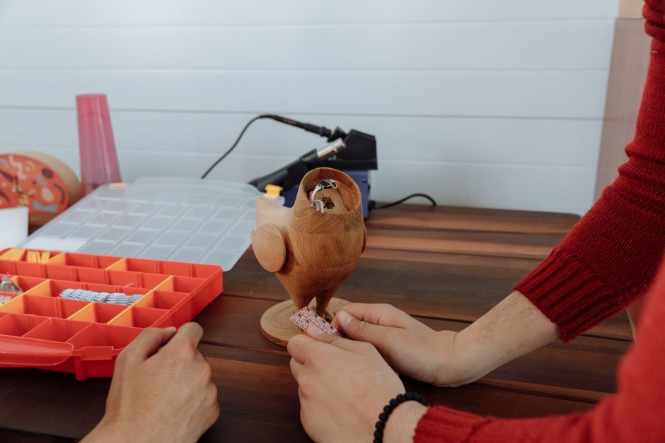 Hands assembling a wooden electronic owl with components on a table.