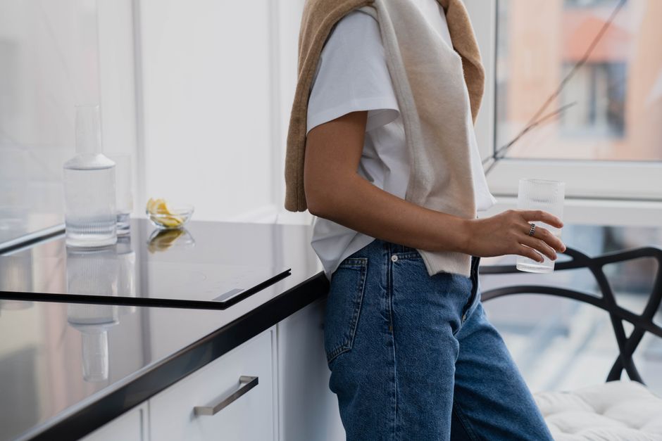 Adult casually leans on a counter holding a glass of water in a modern indoor setting.