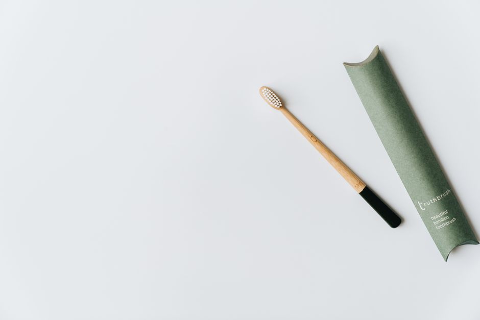 Minimalist bamboo toothbrush with green eco-friendly packaging on white background.